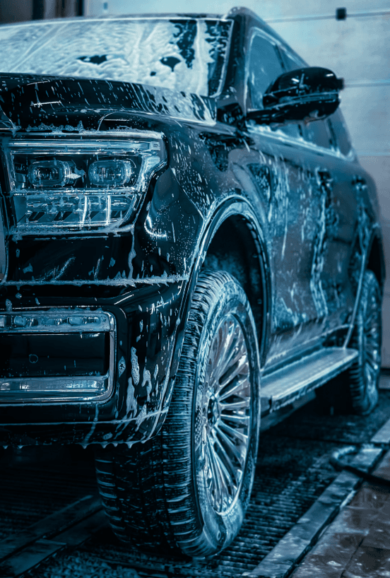 A dark SUV covered in wash foam inside the tunnel
